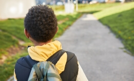 Back view of black child with curly short hair carrying backpack on shoulders
