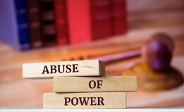 Book spines reading "Abuse of Power" in foreground, gavel in background.