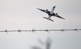 plane flying with barbed wire fence in foreground