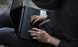 person wearing a hooded sweatshirt typing on laptop