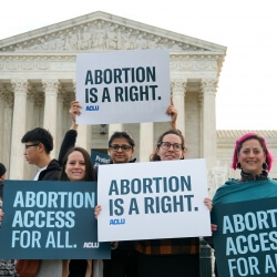 Four people holding signs outside of the Supreme Court that read "Abortion is a right" and "Abortion access for all" 