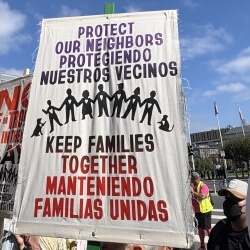 Protest sign reading "Protect our neighbors, keep families together" in English and Spanish
