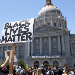 a person is holding a sign that says Black Lives Matter in front of the San Francisco City Hall building