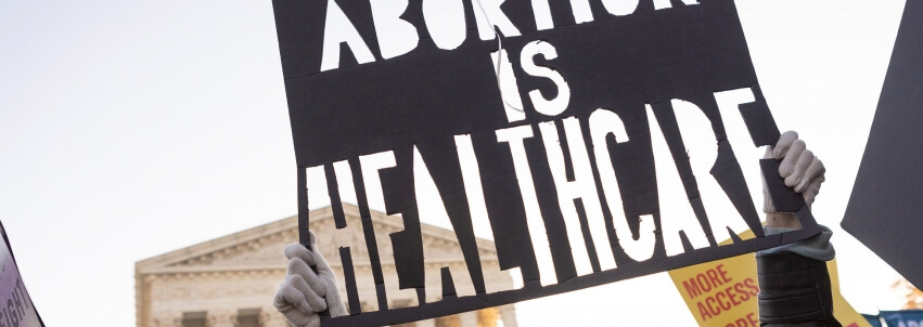 Person holding sign in front of Supreme Court that says "Abortion is Healthcare"