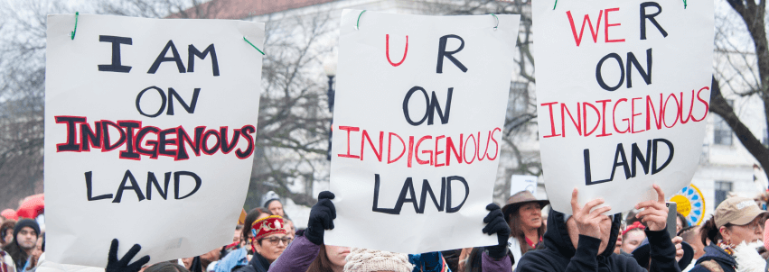 Picture of people holding up three signs. The first sign says "I am on Indigenous land," the second sign says "you are on Indigenous land," and the third sign says "we are on indigenous land."